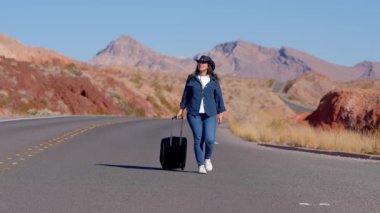 Çölde bavul olarak tek başına yürüyen genç bir kadın. Seyahat fotoğrafçılığı.