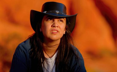 Batı kıyafeti giymiş genç bir kadının Arizona çölünde kırmızı bir kaya kumtaşının üzerinde dinlenirken yakın plan çekimleri. Seyahat fotoğrafçılığı.