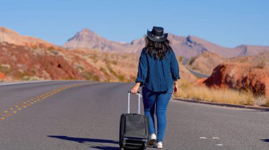 Çölde bavul olarak tek başına yürüyen genç bir kadın. Seyahat fotoğrafçılığı.