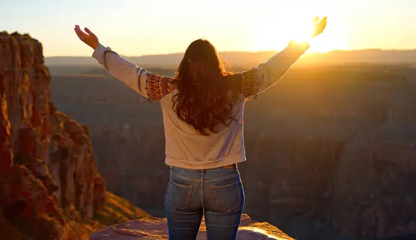 Young woman standing on a cliff at Grand Canyon and raising her arms from a feeling of infinite freedom - travel photography