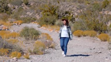 Batı tarzı kıyafetli genç bir kadın Nevada Çölü 'ndeki Red Rock Kanyonu' nda yürüyor. Seyahat fotoğrafçılığı.