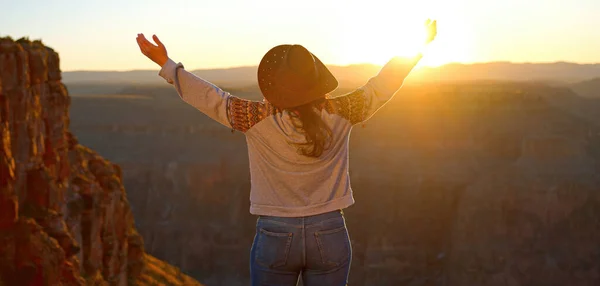 A free-spirited cowgirl stands proudly at the edge of the grand canyon, her jeans blending with the rugged desert landscape as the fiery sunset illuminates her outstretched arms and her soul connects
