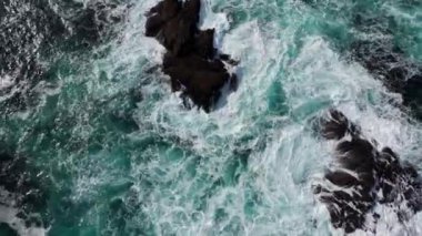 Bir hava görüntüsü canlı turkuaz sularıyla çarpan dalgaların çarpıcı engebeli bir kıyıya çarptığını gösteriyor.