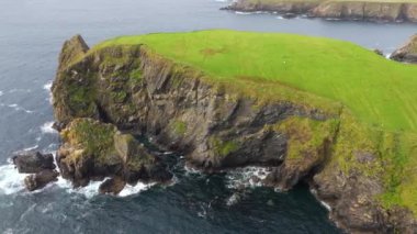 Bulutlu gökyüzünün altında nefes kesen kayalık kıyı şeridi doğanın sükunetini güzel bir şekilde yakalıyor.