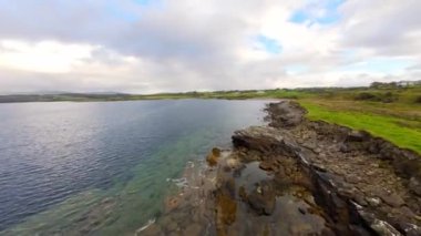 Şaşırtıcı İrlanda - Tipik İrlanda manzarası üzerinde FPV Uçuşu - Sakin bir köy yolu yumuşak bulutlu gökyüzünün altındaki yemyeşil çayırlarda yavaşça kıvrılarak ilerliyor