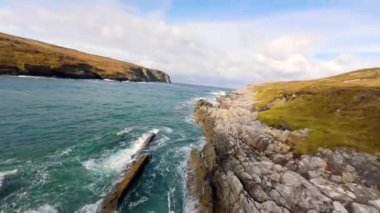 İnanılmaz İrlanda - Arranmore Adası 'ndaki İrlanda batı kıyısında alçak FPV Uçuşu - Bulutlu bir gökyüzünün altında kayalık kıyı şeridinin nefes kesici ve büyüleyici görüntüsü