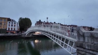 DUBLIN, IRELAND - 12 Ekim 2024 - Hapenny Köprüsü 'nün güzel manzarası bulutlu bir gökyüzünün altındaki sakin nehire yansıyor