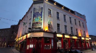DUBLIN, IRELAND - 12 Ekim 2024 - Dublin Tapınak Bar bölgesi - Alacakaranlıkta güzelce aydınlatılmış bir bar, hem yerel halkı hem de ziyaretçileri sıcak bir akşam deneyimi için davet ediyor