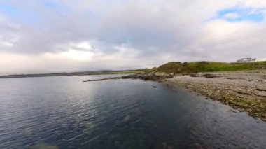 İrlanda 'nın batı kıyısındaki okyanus üzerinde alçak FPV uçuşu- sakin suları gösteren sakin bir manzara bulutlu gökyüzünü güzel yansıtıyor, doğal temalı projeler için mükemmel.