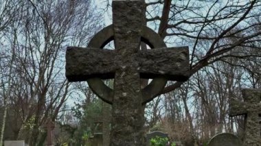 Güzel detaylandırılmış Kelt haçı, ağaçlarla çevrili huzurlu ve huzurlu bir mezarlığın ortasında gururla duruyor. Seyahat fotoğrafçılığı.