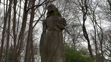 Yıpranmış ve yaşlanmış bir taş melek heykeli zarif bir şekilde çevresini saran canlı ve gür yaprakların arasına yerleştirilmiştir. Seyahat fotoğrafçılığı.