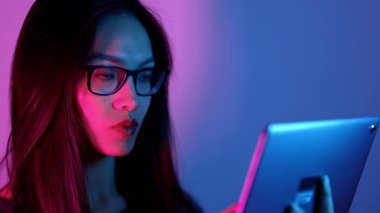 Canlı pembe ve mavi ışıklı tablet kullanan odaklanmış bir kadın modern teknolojiyi iş başında gösteriyor.