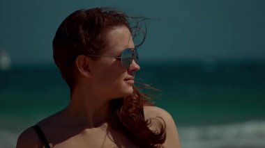 Büyüleyici bir plaj sahnesinde kendine güvenen bir kadın şık güneş gözlüğü takarak dalgalarda eğleniyor.
