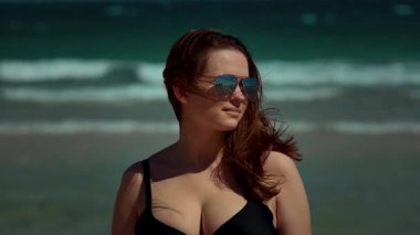Büyüleyici bir plaj sahnesinde kendine güvenen bir kadın şık güneş gözlüğü takarak dalgalarda eğleniyor.