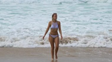 Neşeli ve kaygısız bir kadın büyük bir gülümsemeyle dalgalara doğru mutlu bir şekilde koşuyor.