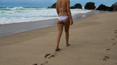 Bir insan güzel sahilde sakin bir şekilde yürür, sıcak güneşin ve yumuşak dalgaların tadını çıkararak kıyıda hafifçe dalgalanır.