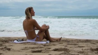 Huzurlu bir kadın, dinginliğin ve sahil hayatı deneyiminin özünü somutlaştıran dalgalara dikkatle bakar.