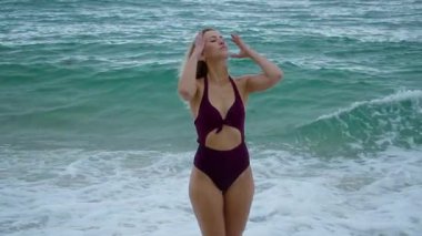 Şık bikinili bir kadın okyanusun kenarında zarif bir şekilde duruyor, sakin ve sakin sahil atmosferinin tadını çıkarıyor.