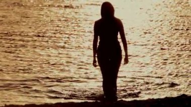 Gün batımında suda yürüyen ve doğadaki sükuneti ve güzelliği yakalayan seksi bir kadının huzurlu bir silueti.