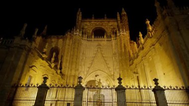 Metal bir çitin arkasında, gece altın ışıkla aydınlatılan Sevilla Katedrali - SEVILLE, SPAIN - 25 Mart 2025