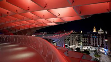 Gece Sevilla 'daki Metropol Şemsiyesi' nin yapısını aydınlatan kırmızı ışıklar ve arka plandaki şehir manzarası - SEVILLE, SPAIN - 25 Mart 2025