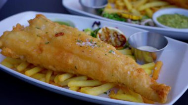 Lezzetli haşlanmış balık ve patates kızartması, limon dilimleri, tartar sosu ve beyaz tabakta yeşil sos.