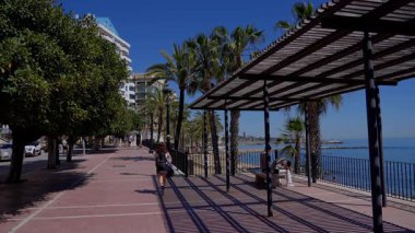 İspanya 'nın Marbella şehrinde güneşli bir günde palmiye ağaçlarının gölgesinde yürüyen kadın - MARBELLA, İspanya - 30 Mart 2025