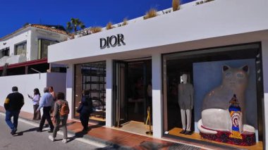 Marbella 'da bir Dior mağazasının önünden geçen yayalar, büyük bir seramik kedi heykeli ve erkek bir mankenle - MARBELLA, SPAIN - 30 Mart 2025