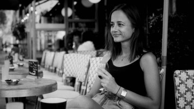 Genç bir kadın Paris, Fransa 'da bir kafede elinde bir bardak şarap tutarken gülümsüyor ve başka tarafa bakıyordu.