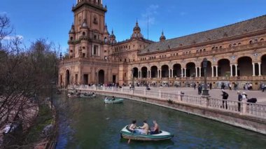 İspanya 'nın Sevilla kentindeki tarihi Plaza de Espana' nın önündeki kanalda güneşli bir günün tadını çıkaran turistler - SEVILLE, SPAIN - 25 Mart 2025