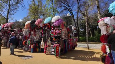Seville, İspanya 'daki bir parkta yelpaze, flamenko elbise ve diğer geleneksel İspanyol ürünleri satan renkli hediyelik eşya standları - SEVILLE, SPAIN - 25 Mart 2025