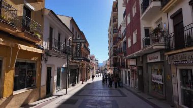 Ronda, Endülüs 'te yaya bir alışveriş caddesinde yürüyen turistler, arka planda mağazalar, balkonlar ve dağlar - RONDA, SPAIN - 28 Mart 2025