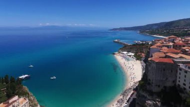 Tropea, Calabria, İtalya 'nın insansız hava aracı görüntüsü, turkuaz sular, kumlu sahil ve güneşli bir yaz gününde tarihi binalar yer alıyor.