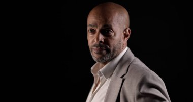 Siyah arka planda poz veren Afro-Amerikan bir iş adamının portresi.