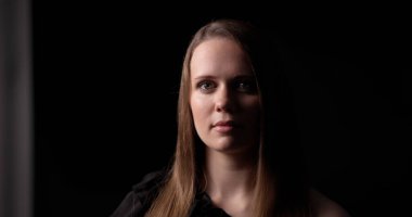 Stüdyo portresi, koyu arkaplan ve gösterişsiz ışıklandırmada ciddi bir ifadeye sahip sarışın bir kadın.