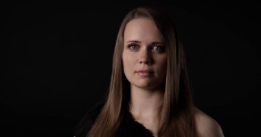 Uzun kahverengi saçlı, siyah giyinmiş, sakin ve kendinden emin görünen beyaz bir kadının stüdyo portresi.