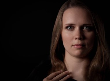 Uzun kahverengi saçlı, yeşil gözlü, koyu renk elbiseli, eli göğsünde genç bir kadının stüdyo portresi.