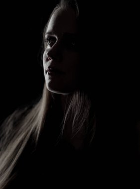 Karanlığın içinden yükselen güzel genç bir kadının dramatik, sade portresi.