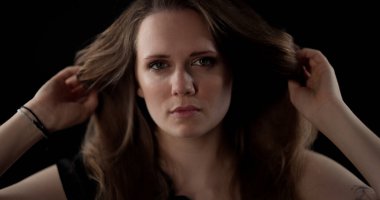 Siyah arka planda saçlarıyla oynayan kendinden emin genç bir kadının portresi.