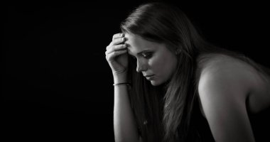 Uzun saçlı, siyah arka planda depresyondan muzdarip genç bir kadın.