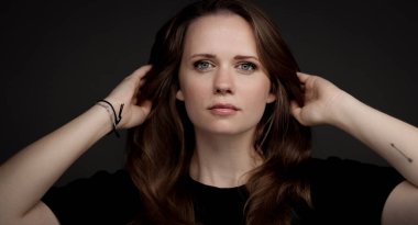 Stüdyo portresi sol kolunda küçük bir ok dövmesiyle uzun kahverengi saçlarına dokunan genç bir kadın.