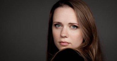 Kendine güvenen iş kadınının portresi başını çeviriyor ve omuzlarının üzerinden gri arka plana bakıyor.