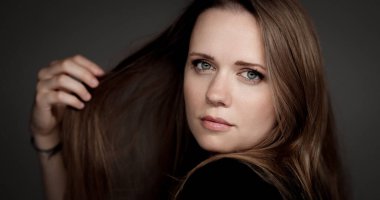 Beyaz saçlı, uzun kahverengi saçlarıyla gri arka planda oynayan beyaz bir kadının stüdyo portresi.