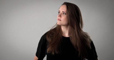 Siyah tişört giyen genç bir kadının düşünceli bir ifadeyle yukarı baktığı bir stüdyo resmi.