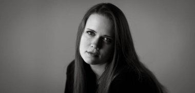 Uzun saçlı güzel bir kadının siyah beyaz portresi. Fotoğraf stüdyosunda gri arka planda poz veriyor.