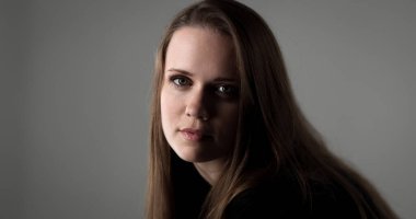 Uzun kahverengi saçlı, siyah balıkçı yaka kazak giyen, gri bir arka planı olan genç bir kadının stüdyo portresi.