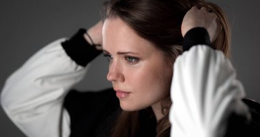 Saçlarını gri bir arka planda düzelten genç bir kadının portresi.