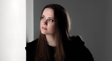 Uzun kahverengi saçlı, siyah giysili düşünceli genç bir kadın. Düşünceli bir ifadeyle yukarı bakıyor.