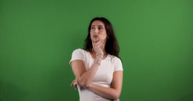 Düşünceli genç bir kadın, eli çenesinde yukarı bakıyor ve yeşil ekran arka planında düşünüyor.