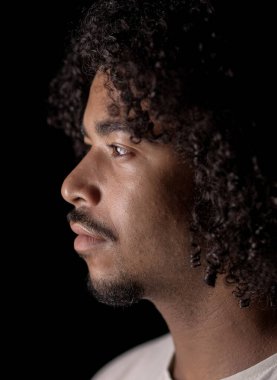 Siyah bir arka plana bakan kıvırcık saçlı ve keçi sakallı Afro-Amerikan bir adamın profili.